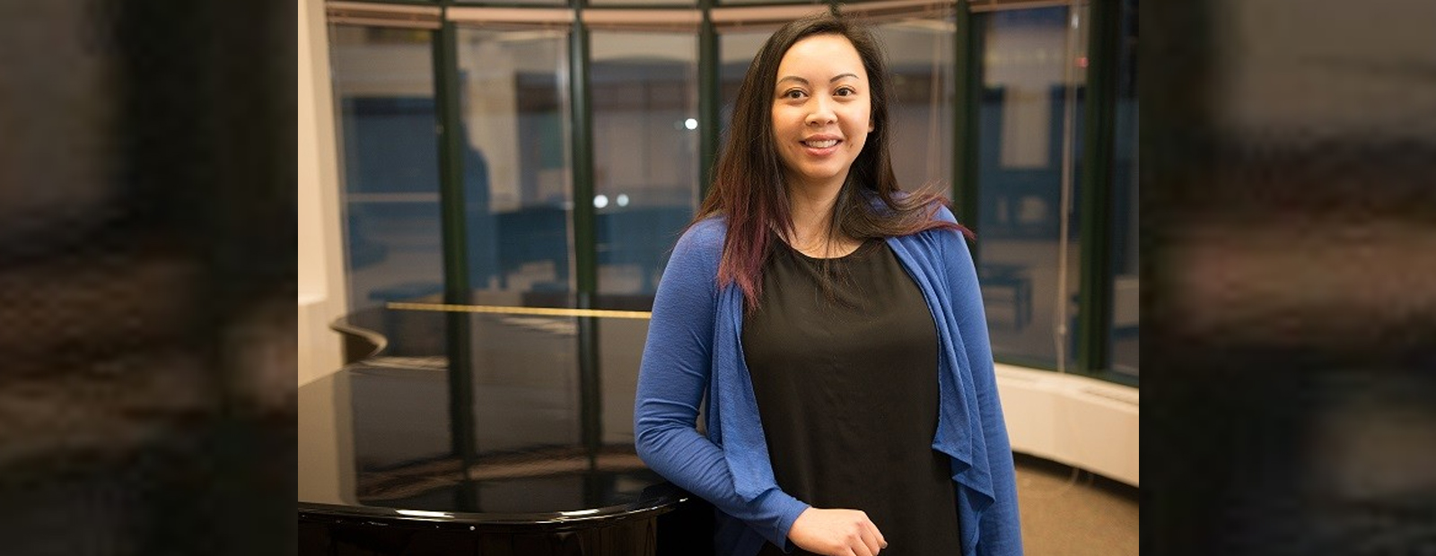 Linh Pham leaning on piano in Alberta College Campus