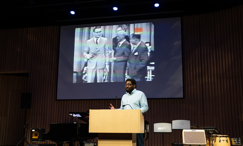 Mboya Nicholson stands in front of screen projecting image of Louis Armstrong