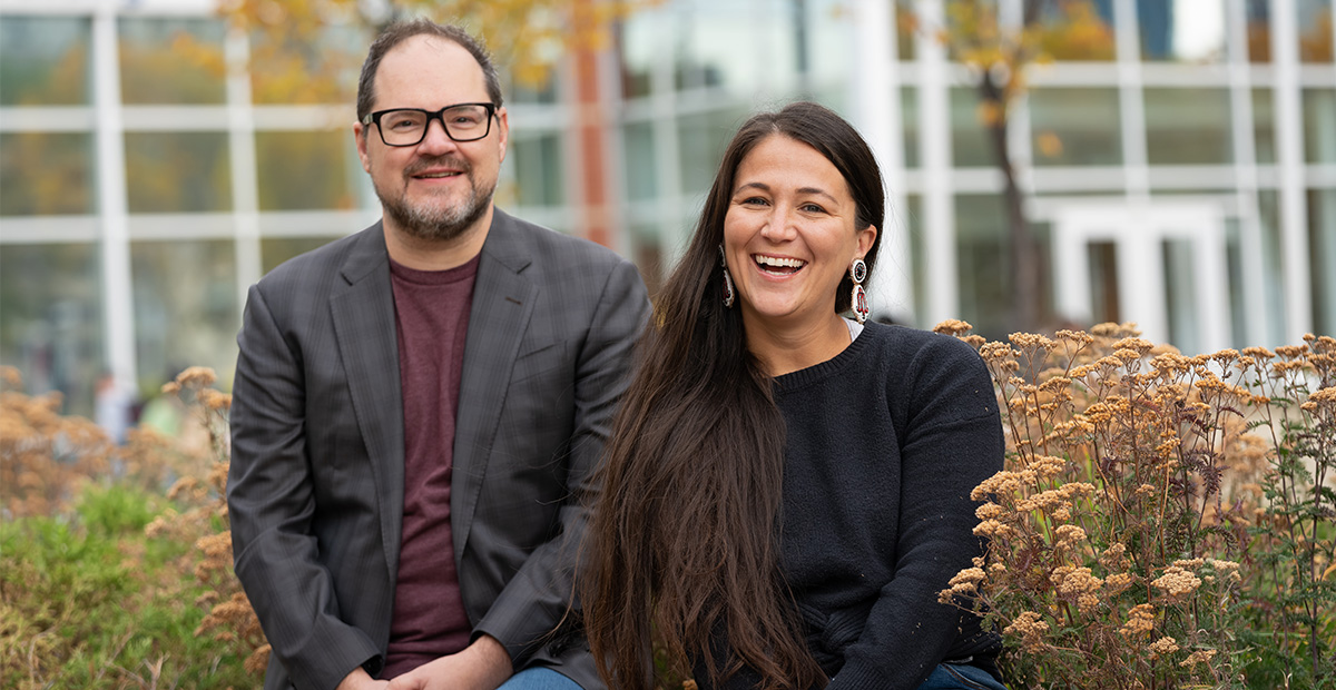 Robert Jennings and Shani Gwin sit together and smile in front of Building 6