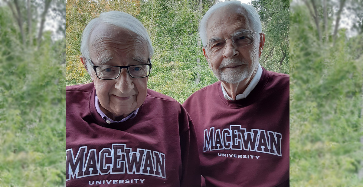 Dr. Terry Flannigan and Dr. Chuck Day stand together in MacEwan sweatshirts in front of a background of trees.