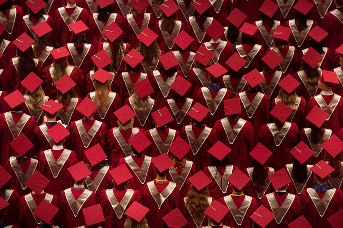 Graduates are seen from behind in maroon caps and gowns