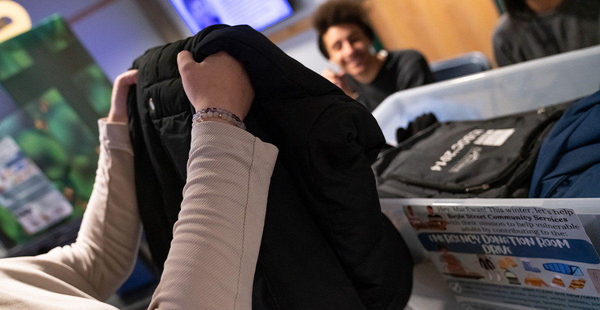 A close-up shot of hands folding a black winter jacket into a plastic donation bin.