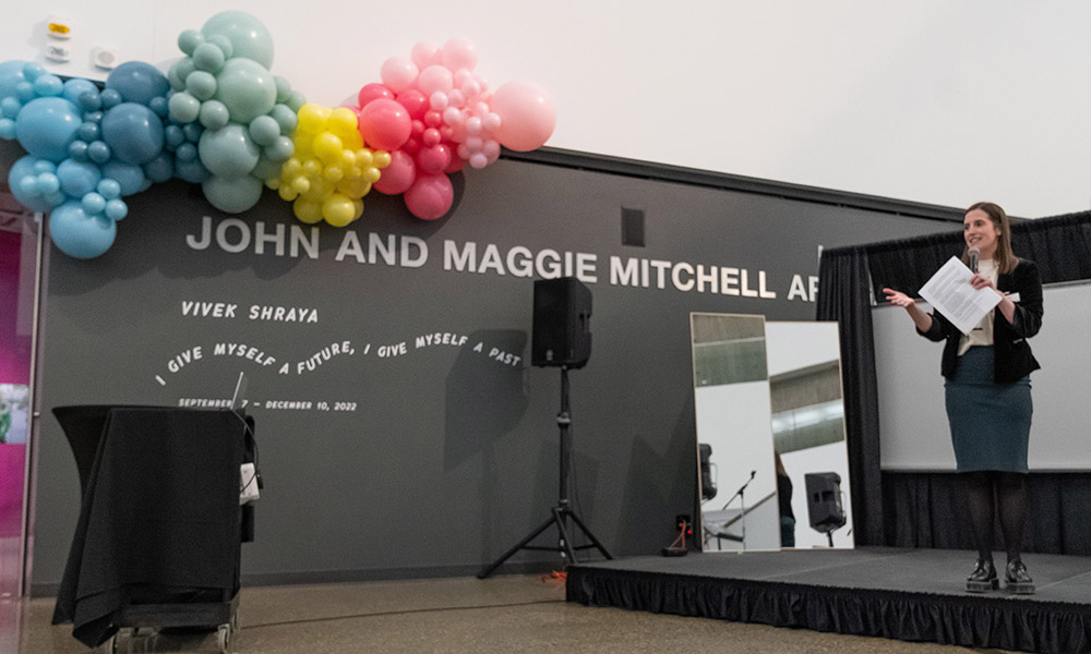 Carolyn Jervis stands at a podium an speaksat the Mitchell Art Gallery's fifth anniversary