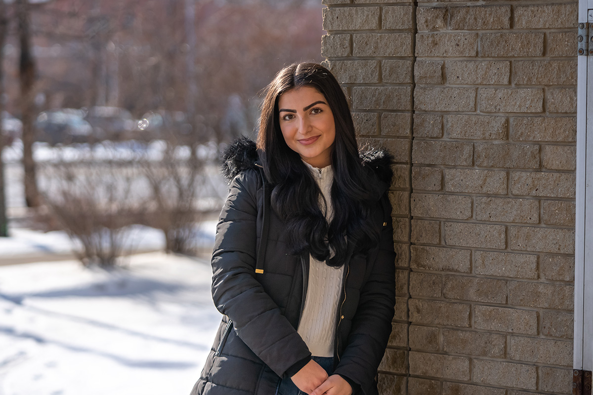 Hazal Ates leans against a brown brick wall and smiles at the camera