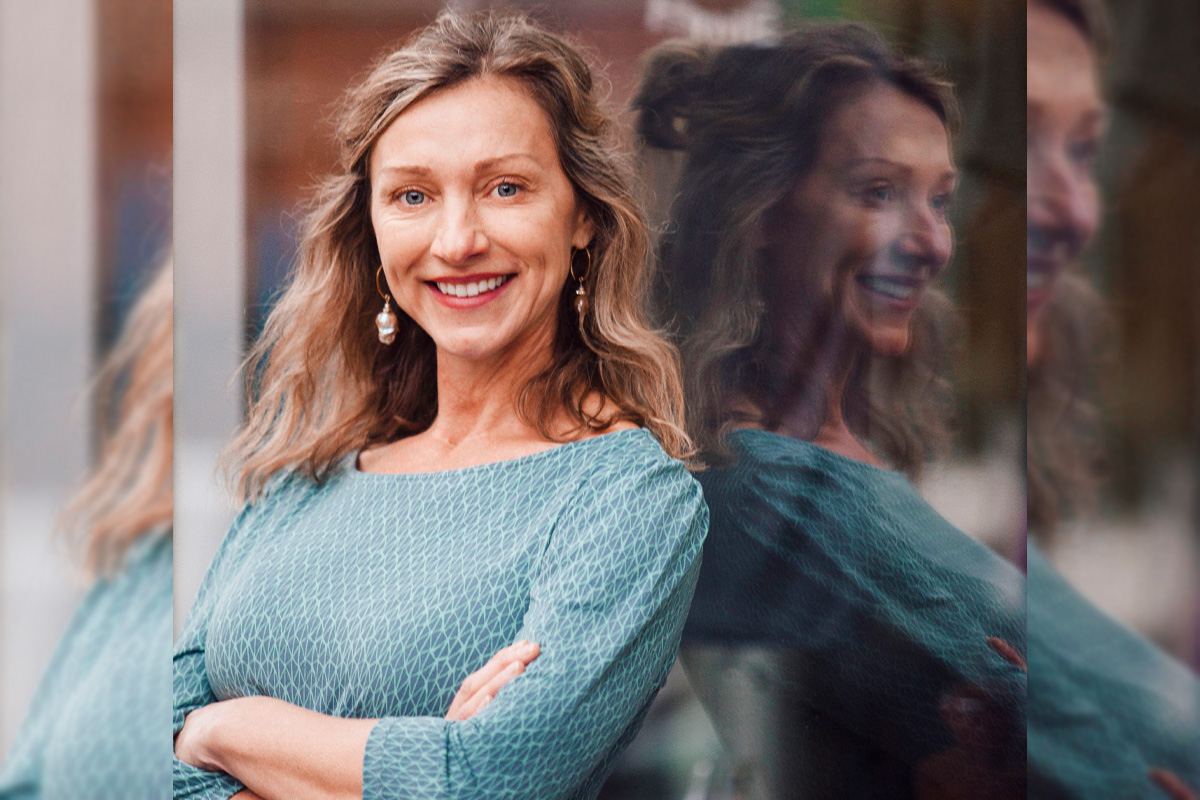 Dr. Leanne Hedberg leans against a glass wall and smiles at the camera