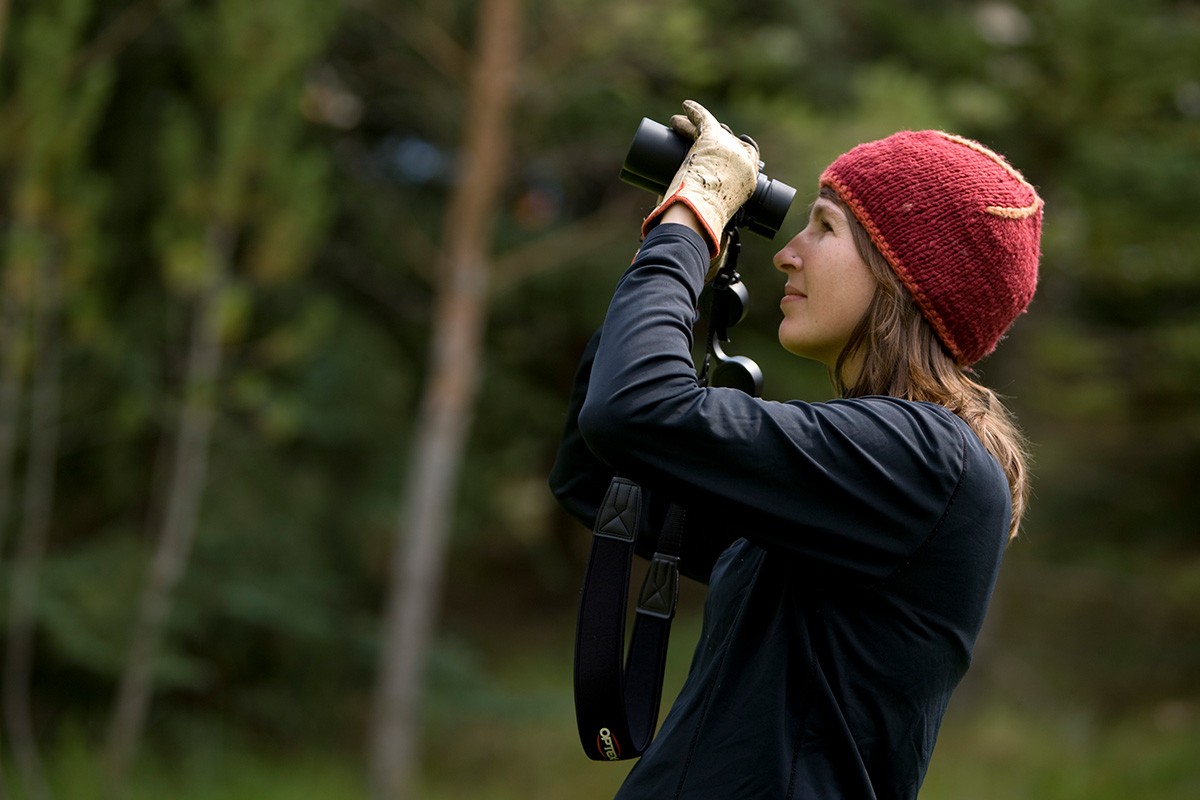 Shannon Digweed looks through binoculars in a heavily wooded area.