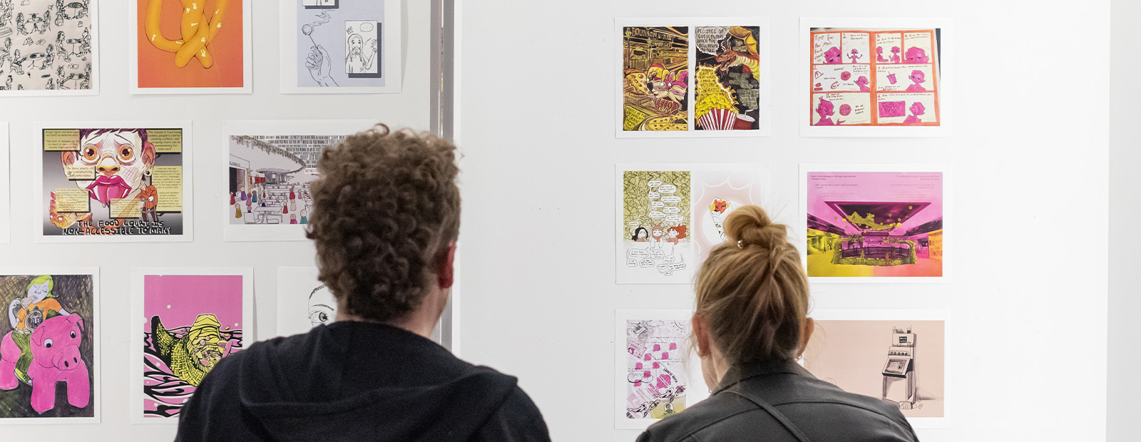 Two people are seen from behind as they look at a display wall of art about mall food.