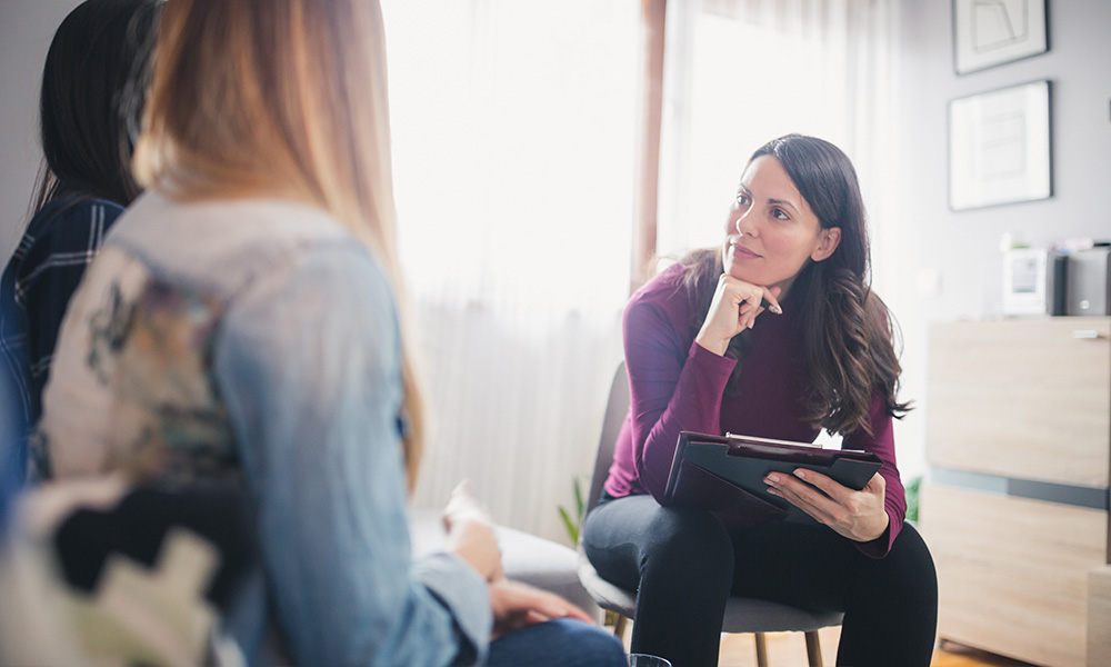 A social worker holds a clipboard and listens to two clients