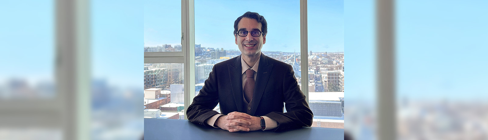 Dr. Farzan Baradaran Rahimi sits at a desk in front of a window with a cityscape in the background