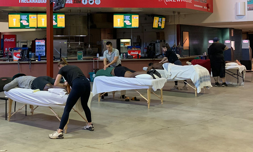 Massage therapy tables lined up on the concourse of Commonwealth Stadium with student providing massage therapy for training camp players