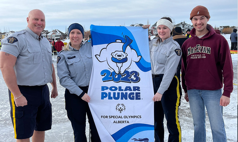 Leduc RCMP detachment officers and McGhee stand with the 2023 Polar Plunge banner out in the cold on Lake Summerside