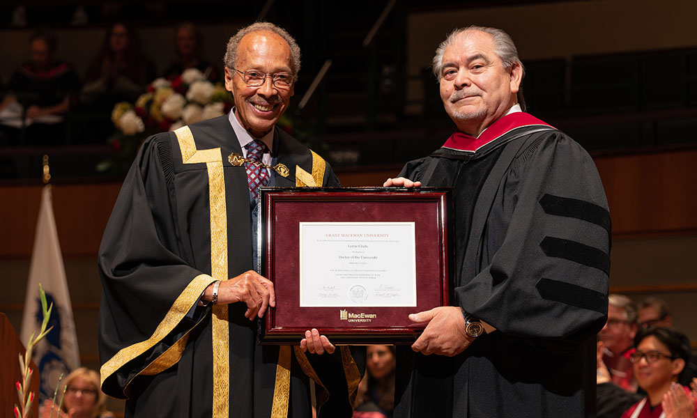 Dr. Anthony Fields and Lorne Gladu on stage holding a frame with Gladu's honorary doctorate parchment