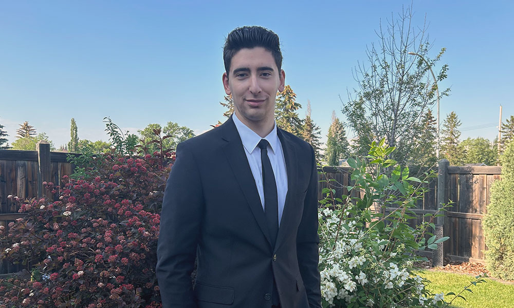 Anthony stands in front of a background of flowering shrubs