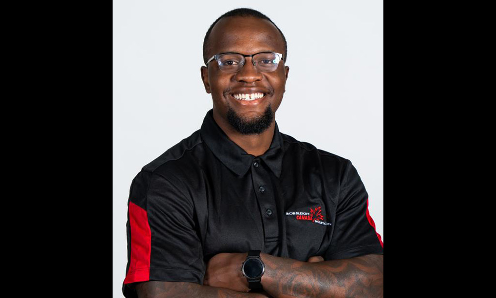 Kenny M'Pindou with arms crossed wearing a Bobsleigh Canada collared shirt