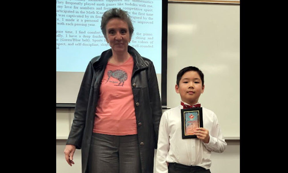 Dr. Cristina Anton and Patrick Li stand in front of a screen. Patrick holds his award.