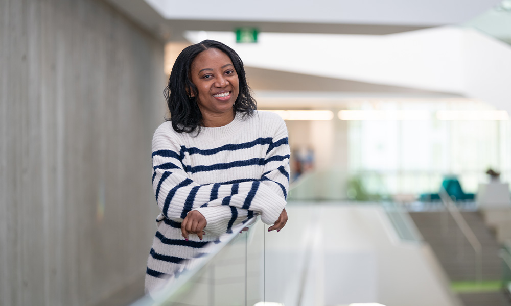 Tracy Thomas stands in Allard Hall wearing a striped sweater