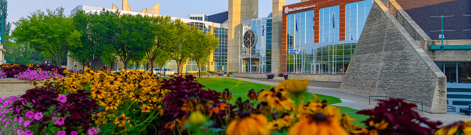 A fall photos of the main campus entrance with flowers yellow, orange and pink flowers in the foreground with a blue sky in the background