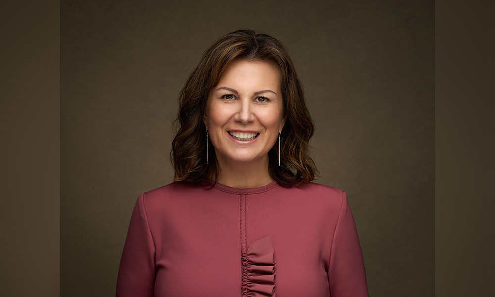 Nicole Bourque-Bouchier smiles while standing against a taupe bckground