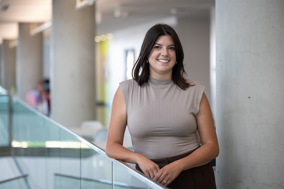 Kayli Avveduti stands in Allard Hall, leaning against a glass railing in a headshot