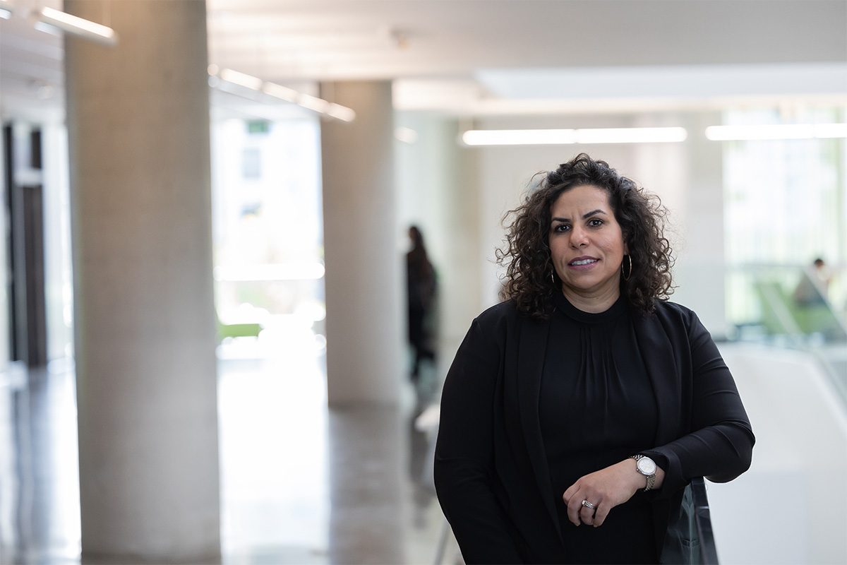 Youssra Badr stands in Allard Hall, leaning on a glass railing. She wears a black shirt under a black blazer