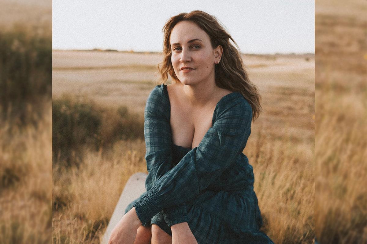 Mallory Chipman sits in a field of wheat, leaning forward so her arms rest on her knees