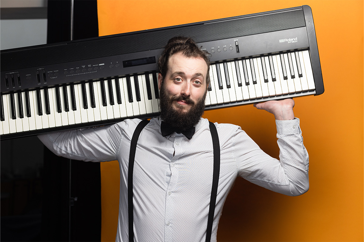 Byron Martin wears a white shirt and black suspenders, and holds an electric keyboard on his shoulders.