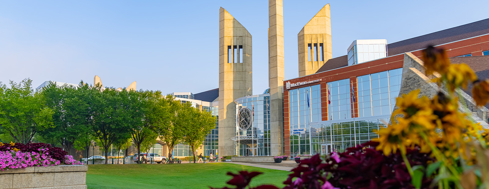 A photo of the clocktower entrance to Building 7 with blue sky in the background and yellow flowers in the foreground.