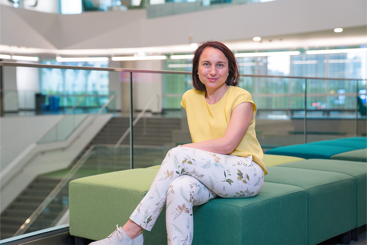 A woman wearing a yellow shirt and white pants sits on a cushioned cube in Allard Hall