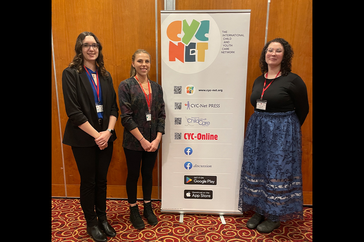 Three women stand around a banner for the Child and Youth Care Network.