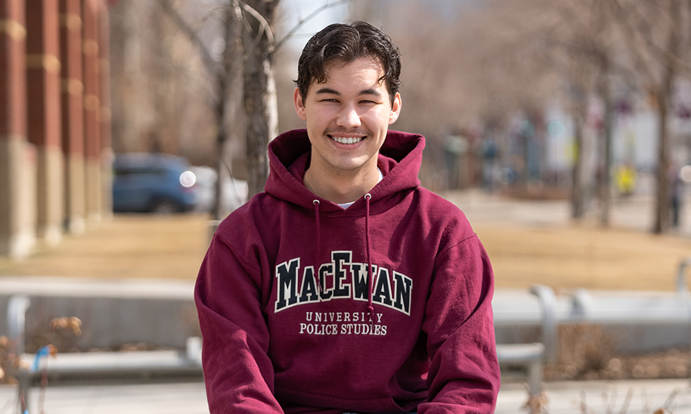 Connor McGhee wears a MacEwan hoodie and sits outside campus