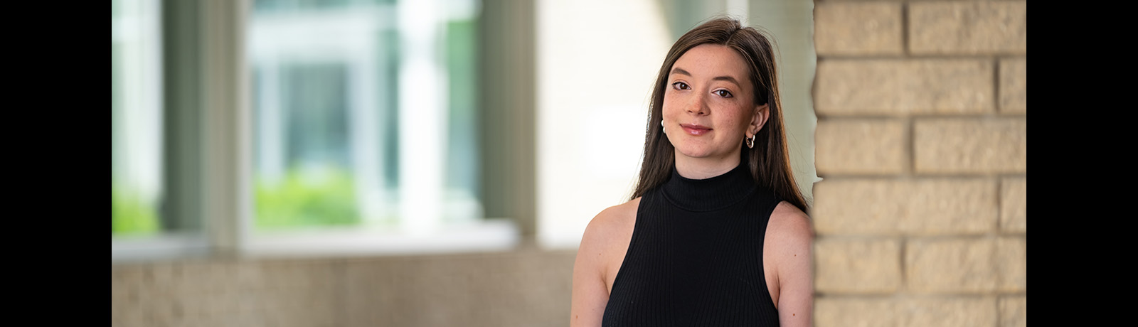 Kateryna Kuzmuk stands beside a brick column on MacEwan's campus.