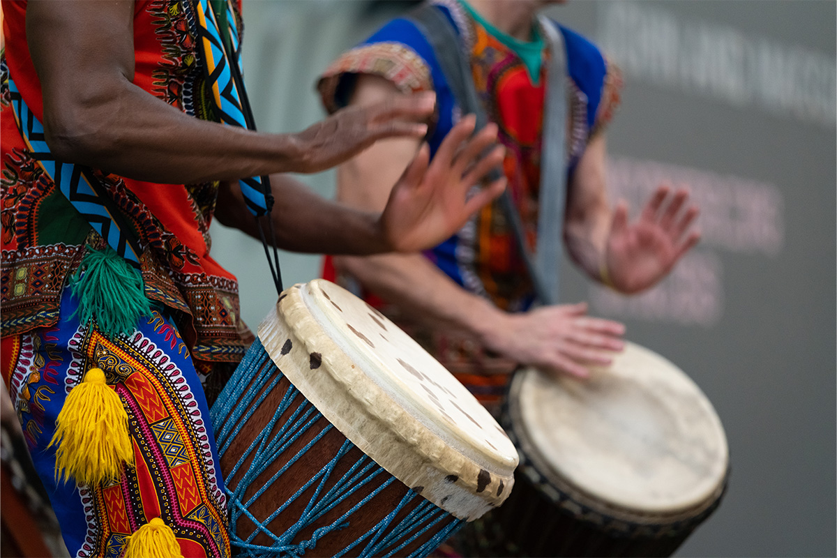 A close-up of hands drumming on a drum with colourful adornments