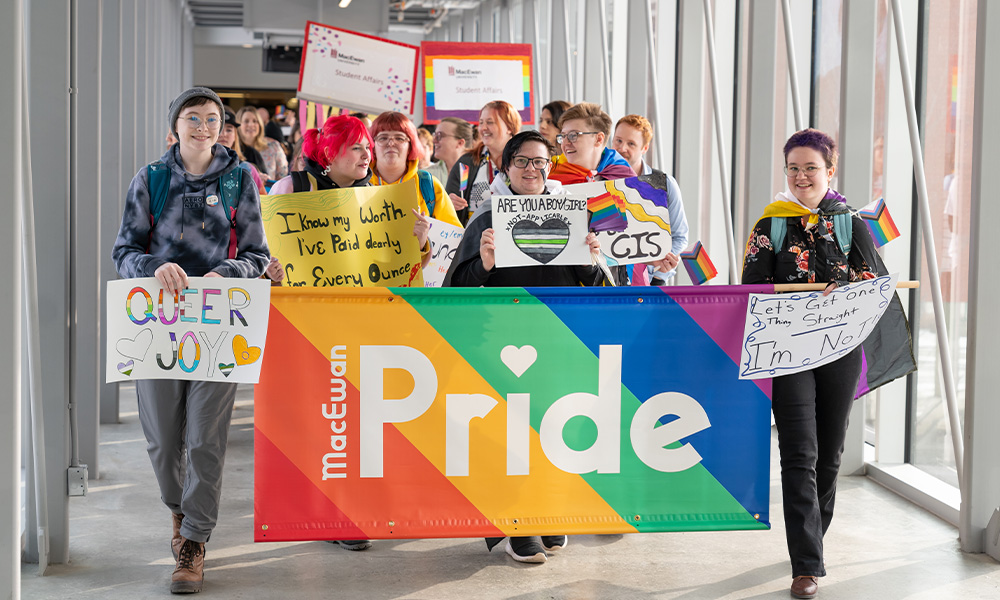 Students, staff and faculty carry a Pride banner as they march through the pedway between Building 9 and Allard Hall.