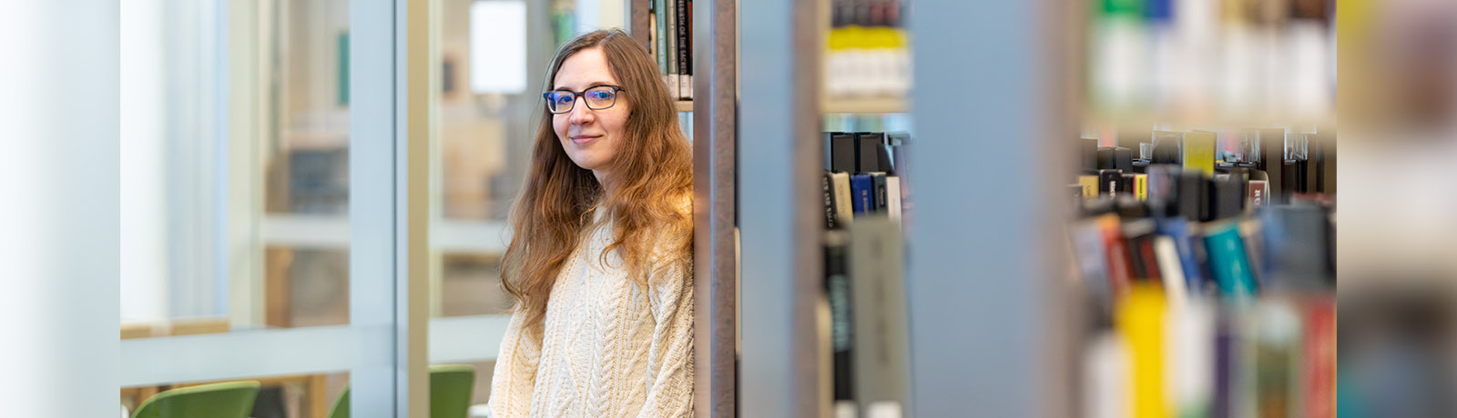 Ashley Platz leans against a bookshelf in the MacEwan Library