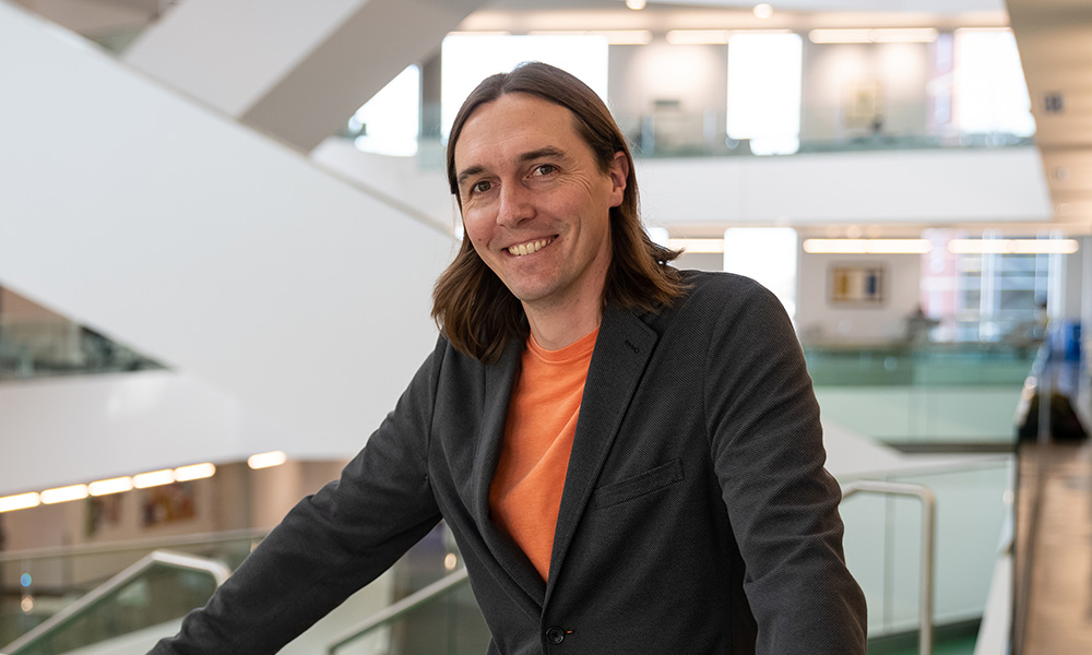 Dr. Trevor Hamilton leans against a railing in Allard Hall