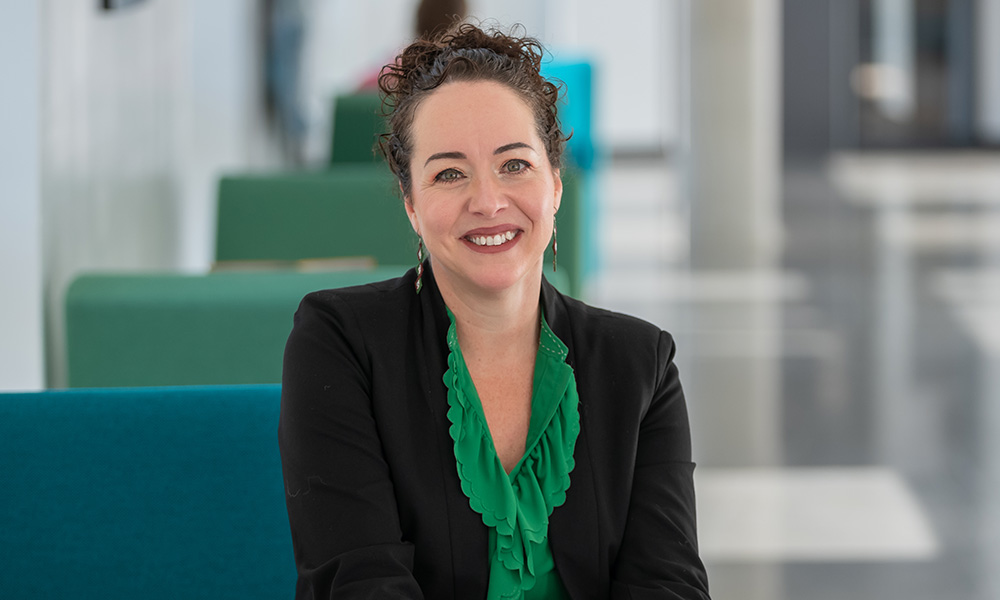 Dr. Melissa Hills sits on a green chair in Allard Hall