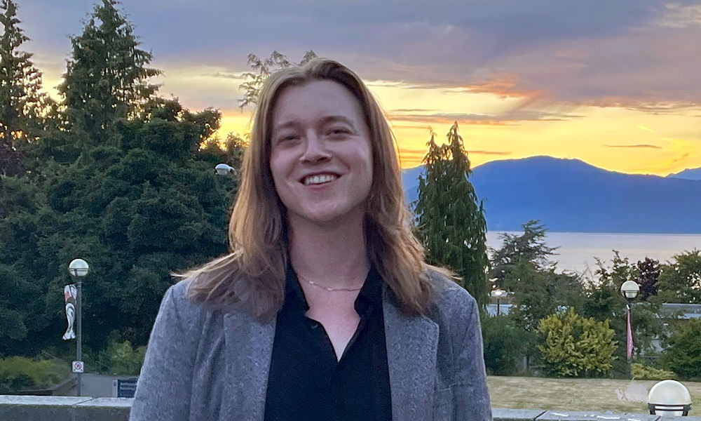Myles stands smiling with mountains and a sunset in the background