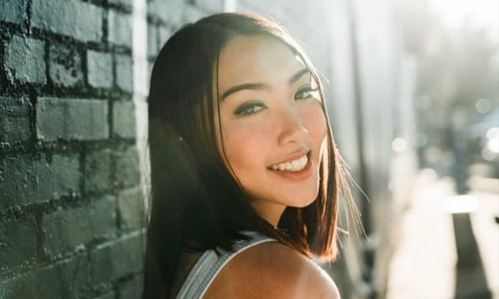 Ivy Phuong Ho smiles while leaning against a brick wall