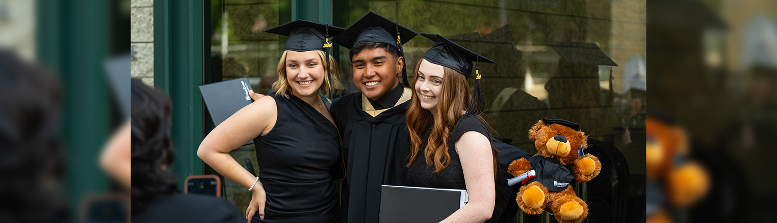 Three friends wearing grad caps and black robes pose for a photo.