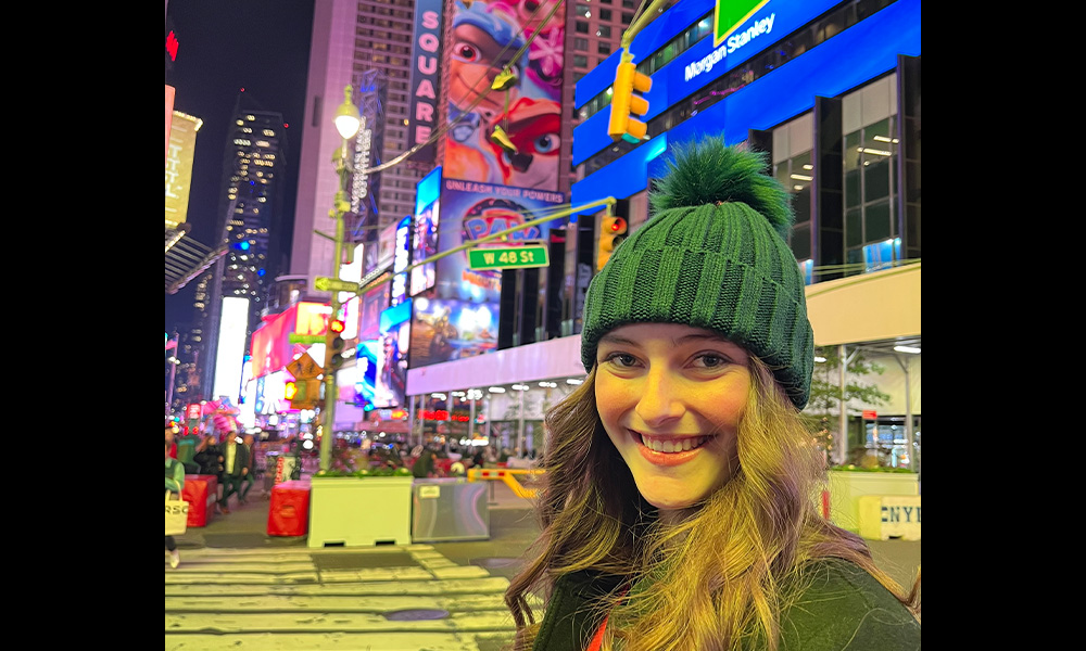 A woman wearing a green toque stands in Times Square.