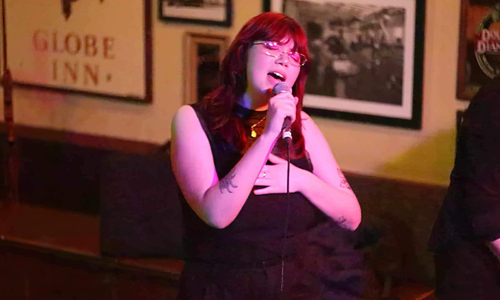 A woman with red hair sings into a microphone.