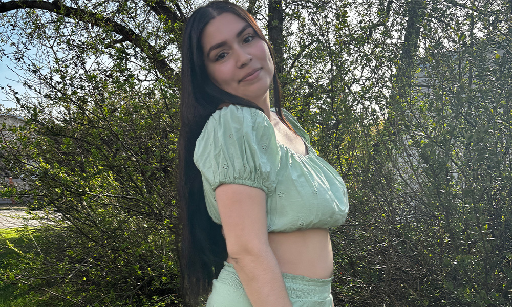 A woman in a green crop top poses in front of trees.