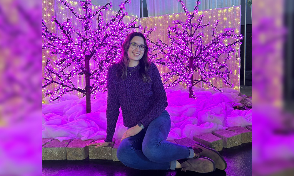 A woman sits in front of a display of purple Christmas lights.