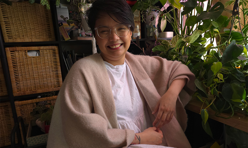 A woman wearing glasses and a beige cardigan sits in a large armchair