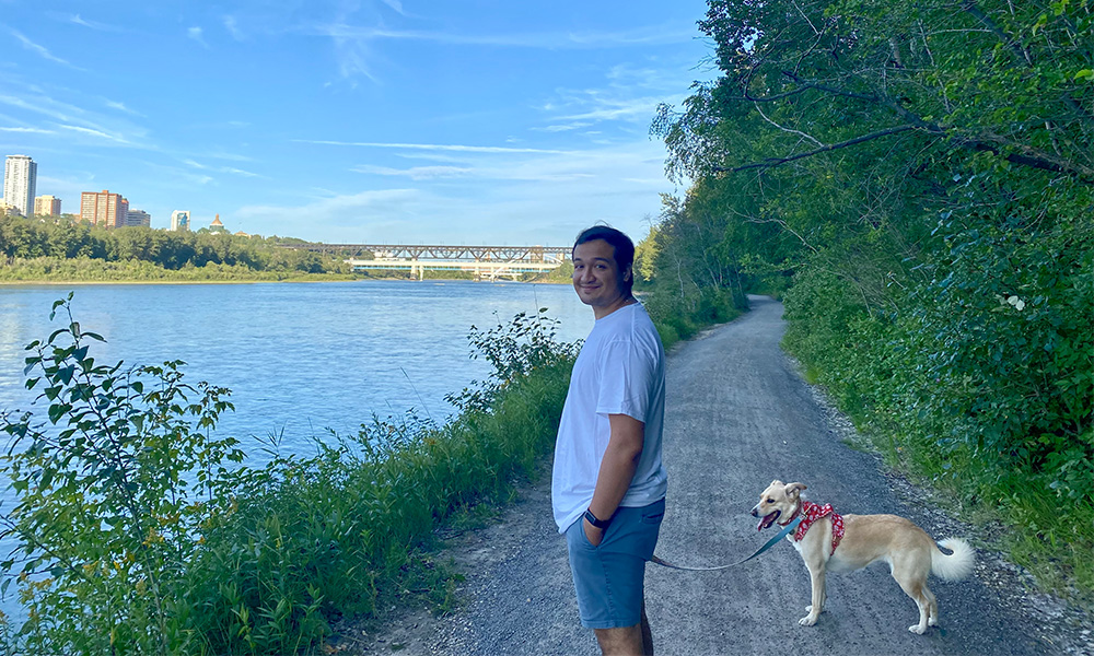 A man walks his dog along a paved path near the river.