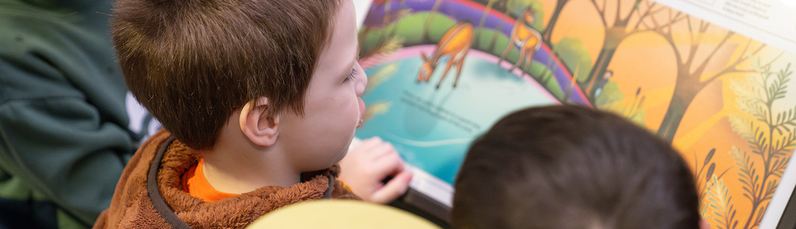 Children gather around a StoryWalk sign with colouful pages from a children's book