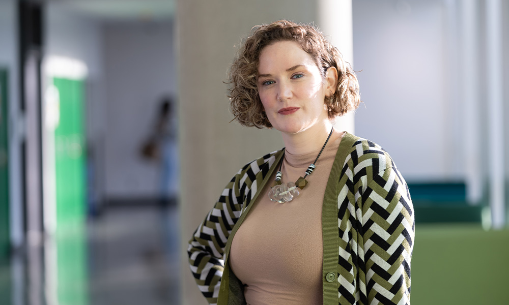 Sheena Rossiter stands in Allard Hall, wearing a patterned cardigan over a beige shirt.