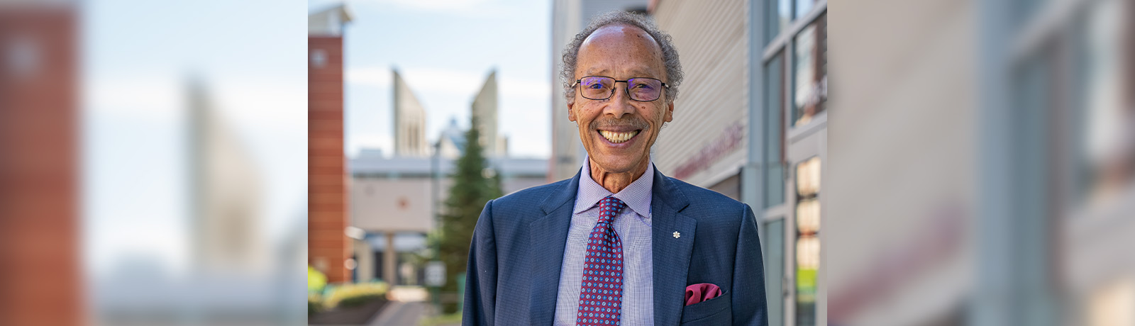 Dr. Fields stands outside of Building 9 on campus wearing a navy blue suit.