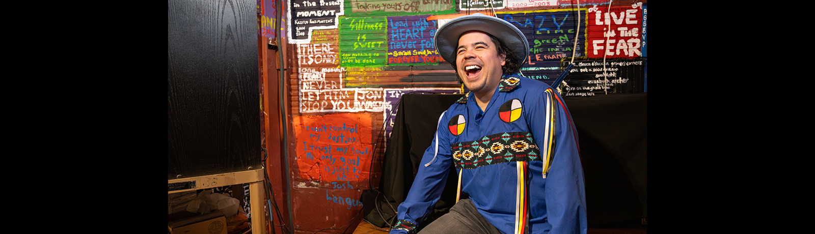 Josh Languedoc in front of a wall covered with hand-painted quotations by students.