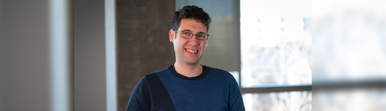 Dr. Miller wears a blue shirt and glasses and smiles.